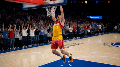 NBA篮球比赛现场，球员在空中完成扣篮动作，观众席气氛热烈